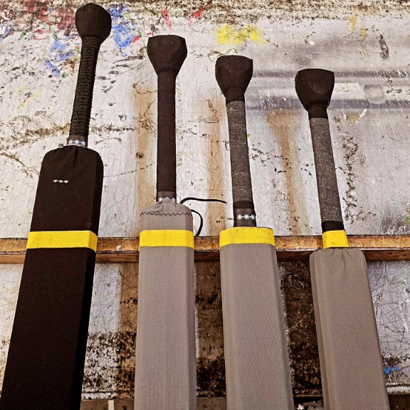 4 swords marked with yellow tape resting on a thin piece of wood to show their different balance points.
